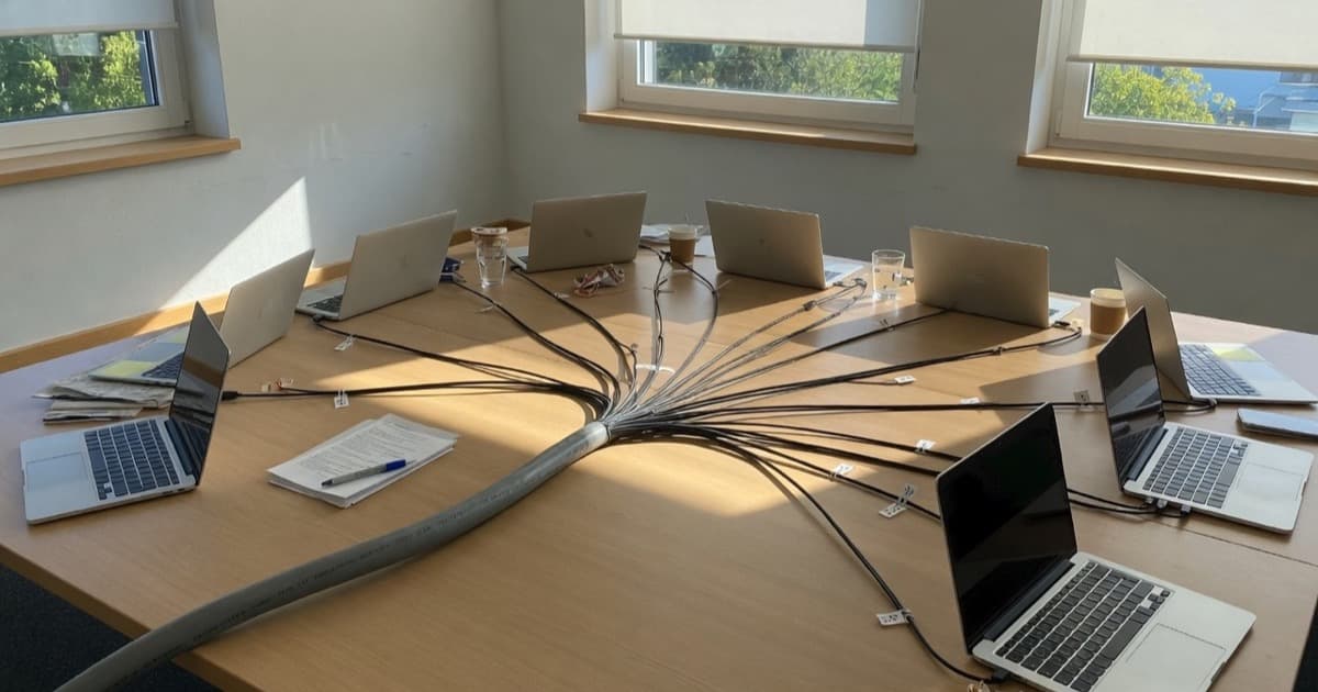 Konferenzraum: ein dickes Kabel verzweigt sich zu mehreren Laptops – Symbol für zustandslose MCP-Architektur